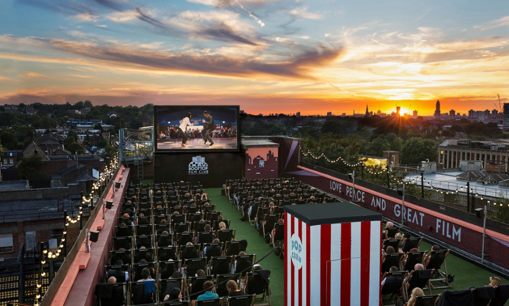 People in deckchairs watching a film on a big screen on a rooftop